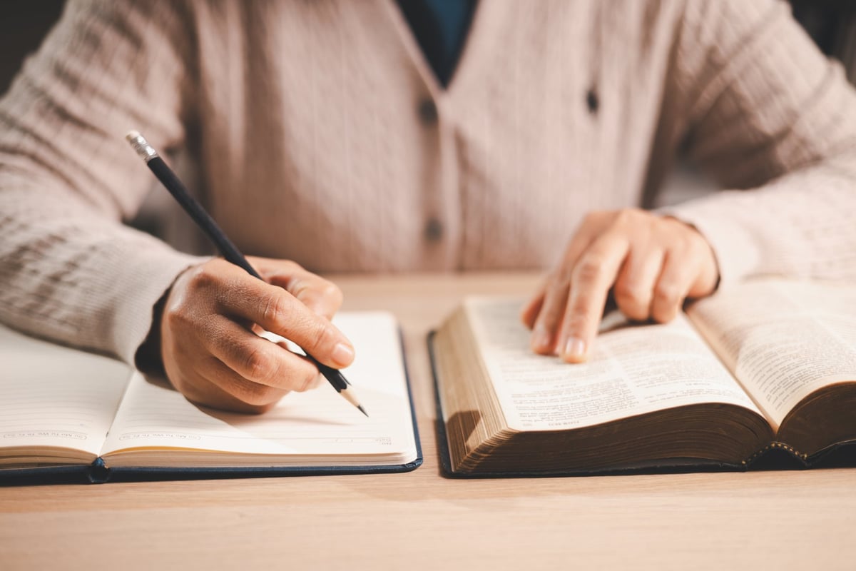 Hands taking notes in a notebook while studying an open Bible